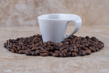 Neatly arranged coffee bean pile surrounding a cup of coffee on marble background