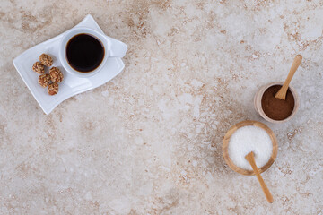 Sugar, ground coffee powder, a cup of coffee and glazed peanuts on marble background