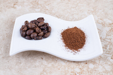 Coffee beans and ground coffee powder on a fancy platter on marble background