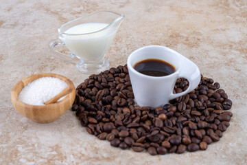 Small bowl of sugar next to a coffee bean pile surrounding a cup of coffee on marble background