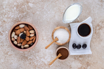 A bowl of assorted nuts, small bowls of milk, ground coffee, sugar and a cup of coffee on marble background