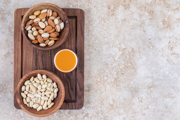 Bowls of nuts and a cup of juice on a board on marble background