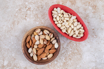 Bowls of almonds, pistachios and un-hulled peanuts on marble background