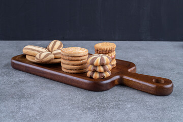 A wooden board with a variety of cookies bundled together on marble background