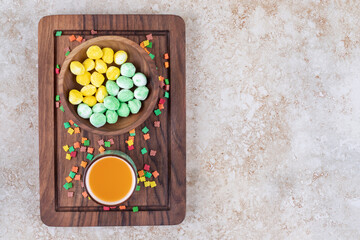 A bowl of mint and lemon candies and a cup of juice on a wooden board on marble background