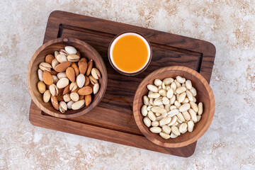 Bowls of nuts and a cup of juice on a board on marble background