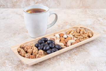 Piles of candy and various nuts in a small tray next to a tea mug on marble background