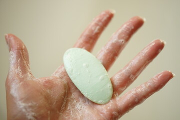 Wet female hand hold green bar of soap on a beige background