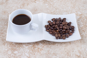 A small cup of coffee next to a pile of coffee beans on marble background