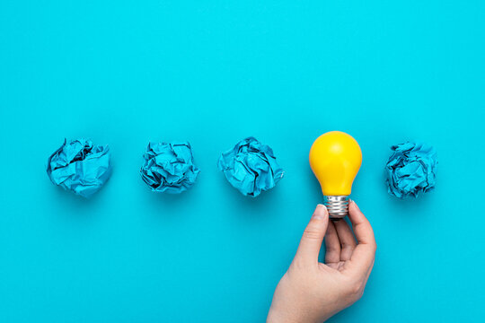 One person have great idea during brainstorming session concept. Great idea concept with bulb in hand and crumpled office paper. Conceptual photo of light bulb in human hand over turquoise background.