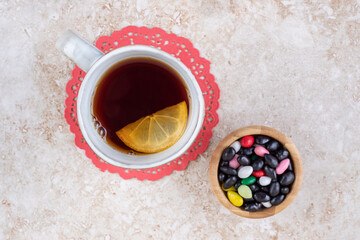 A cup of tea on a doily and assorted candy serving on marble background