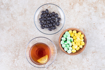 A variety of candies served next to a cup of tea on marble background