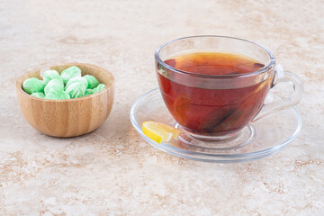 A cup of tea and a bowl of mint candies on marble background