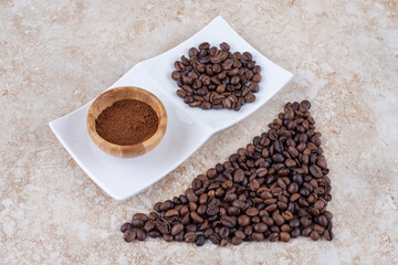 Coffee bean piles and a small bowl of ground coffee on marble background