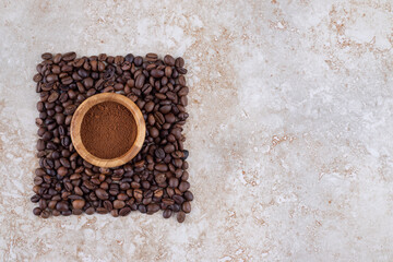Small bowl with coffee powder surrounded with a small pile of coffee beans on marble background