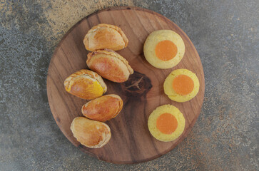 Cookies, marmelades and small buns on a board on wooden background