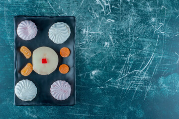 Cookies and marmelades around a white chocolate topped cake on a platter on blue background