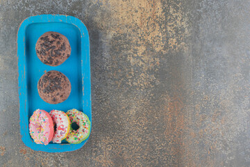 Chocolate cookies and small donuts on a blue platter on wooden background