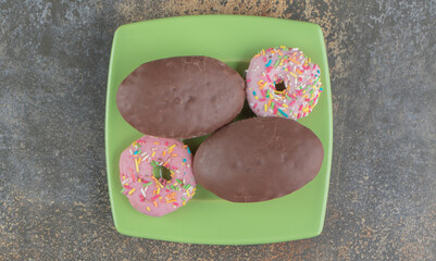 A donut and chocolate coated cakes on a platter on wooden background