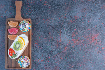 Fruit topped cake with cupcakes and marmalades in a small tray on abstract background