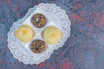 Snack-size donuts and cookies on a serving platter on a doily on abstract background
