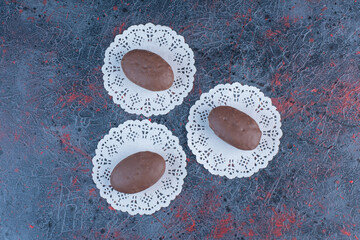 Chocolate coated cakes on doilies on abstract background