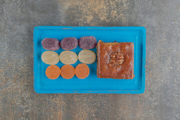 Marmelades next to a piece of bakhlava on a blue platter on wooden background