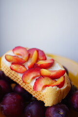 Sandwich with plum slices in a plate with plums.