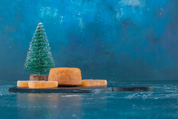 Jelly filled cake, marmelades and a tree figurine on a black board on blue background
