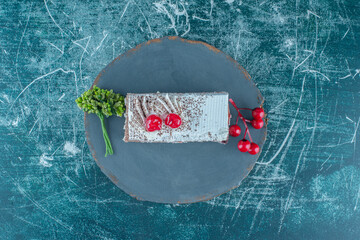 A slice of cake with cherry topping on a wooden board on blue background