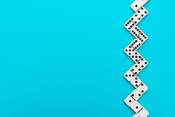 Domino pieces forming zigzag on turquoise blue background with copy space. Flat lay minimalist photo of domino bones.