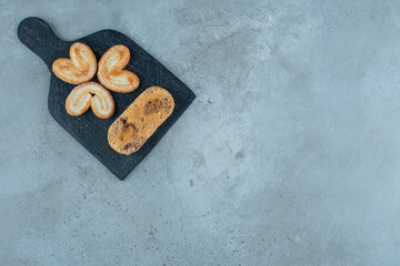 Flaky cookies and a small cake on a board on marble background