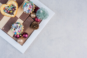 Cupcakes and a heart cake on a bunch of wafers next to christmas baubles on marble background