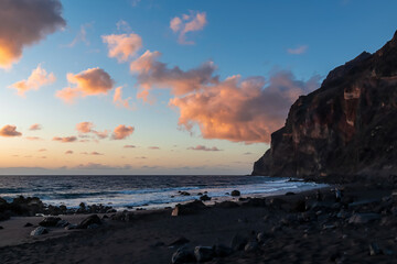 Scenic view during sunset on the volcanic sand beach Playa del Ingles in Valle Gran Rey, La Gomera, Canary Islands, Spain, Europe. Massive cliffs of the La Mercia range. Calm atmosphere at the seaside