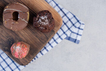 cupcakes and a donut on a wooden board on marble background