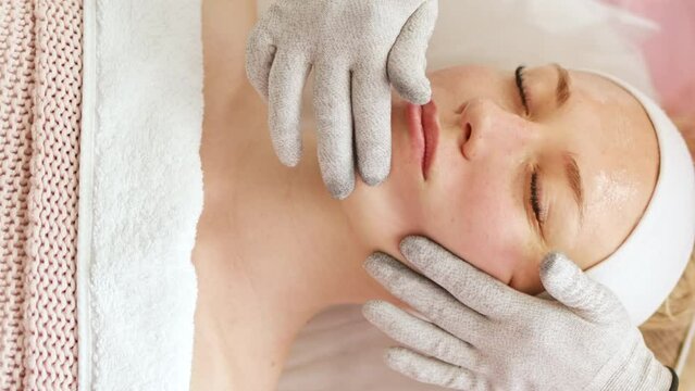 Beautician cosmetologist makes a procedure on the face with microcurrent therapy gloves. Hardware cosmetology in clinic salon for client.	