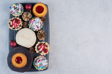 Delectable dessert arrangement on a navy board adorned with baubles and pine cones on marble background