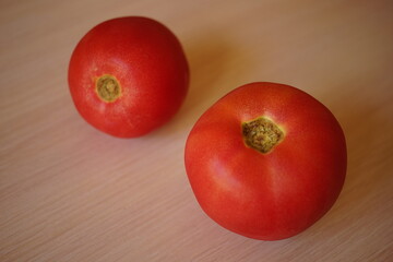 Two ripe pink tomatoes on pale wooden table