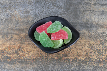 Black bowl full of marmelades on wooden background