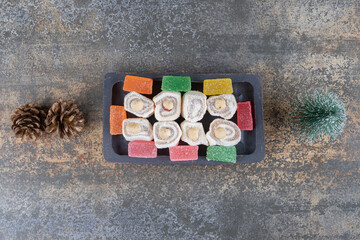 Small tray of marmelades and turkish delights next to christmas decorations on wooden background