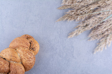 Fototapeta na wymiar Sesame coated strucia loaf next to stalks of dried feather grass on marble background