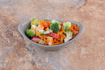 Oval bowl of mixed vegetable salad displayed on marble background