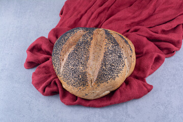 Piece of cloth under a loaf of black sesame coated bread on marble background - obrazy, fototapety, plakaty