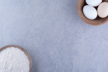 Bowls of egg and flour on marble background