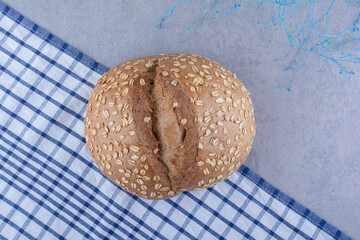 Flake covered loaf of bread on a laid-out towel on marble background
