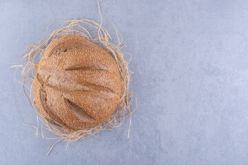Single bread loaf sitting on a straw pile on marble background