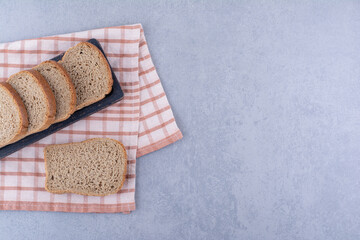 Tray of sliced brown bread on a folded towel on marble background