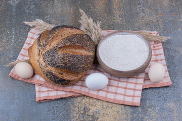 Bowl of flour, eggs and sesame coated bread on a towel on marble background