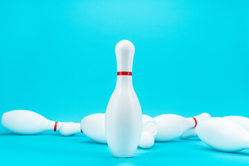 Minimalist photo of bowling pin over turquoise blue background. One standing white bowling pin in front of knocked down pins. Bad times finacial business survival concept.