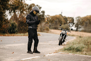 motorcyclist typing message in smartphone wearing gloves, custom motorcycle cafe racer.